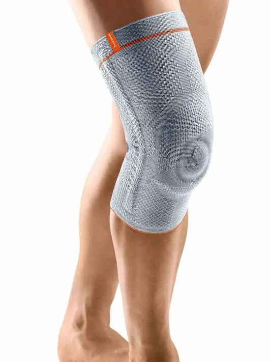 Die Abbildung zeigt die Sporlastic GenuHit Kniebandage, eine elastische Bandage zur Stabilisierung des Kniegelenks. Sie ist aus grauem, atmungsaktivem Material gefertigt und besitzt seitliche Stabilisierungsstäbe sowie eine ringförmige Pelotte, die die Kniescheibe umschließt. Die Bandage bietet gezielte Unterstützung bei Instabilitäten und Kniebeschwerden.